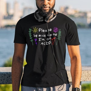 May include: A black t-shirt with a colorful graphic that says "Please be nice to me I'm on ACID". The graphic is drawn in a childlike style with a sun, flowers, and butterflies.