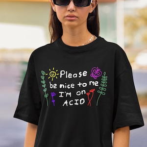 May include: Black t-shirt with a white graphic that says "Please be nice to me I'm on ACID" with a sun, butterfly, and flowers drawn around the text.
