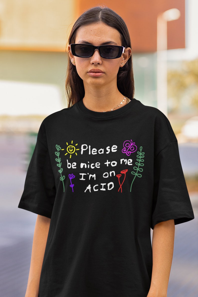 May include: Black t-shirt with a white graphic that says "Please be nice to me I'm on ACID" with a sun, butterfly, and flowers drawn around the text.
