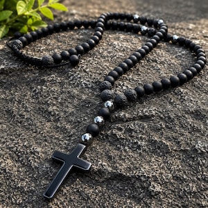 Peut inclure: Un chapelet composé de perles noires mates lisses, de perles en pierre de lave poreuse texturée et de perles intercalaires métalliques argentées polies. Le collier se termine par un pendentif croix noir uni, lisse et brillant.