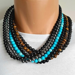May include: A collection of beaded necklaces in various colors and textures. The necklaces include black, gray, turquoise, and brown beads. The beads are arranged in multiple strands, creating a layered effect. The necklaces are displayed on a mannequin.