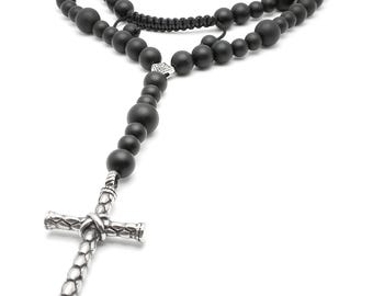 May include: A black beaded rosary with a silver-colored cross pendant. The beads vary in size and are strung together. The cross has a textured design. The rosary is displayed against a white background.