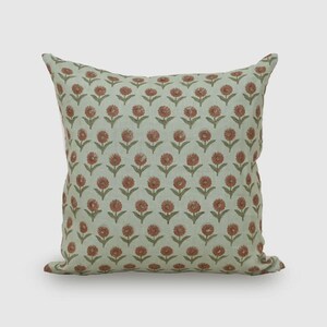 May include: A square throw pillow featuring a repeating pattern of small, rust-colored floral motifs on a light sage green background. The design consists of evenly spaced, stylized flowers with green stems and leaves arranged in a grid-like layout.