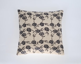May include: Square beige throw pillow with a repeating pattern of black floral designs. The pillow has a neutral color palette and a simple, elegant aesthetic, suitable for home decor.
