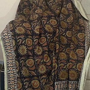 Könnte beinhalten: Eine schwarze und beige Wurfdecke mit einem Blumenmuster. Die Decke hat einen Fransenrand und ist aus einem weichen, komfortablen Stoff gefertigt.