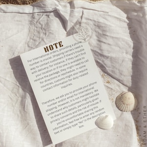 May include: A white card with the word "NOTE" printed at the top, with text about international orders and contact information. Two seashells are next to the card on a white cloth.
