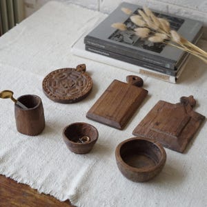 May include: A collection of handcrafted wooden kitchen and home decor items. Includes a small cutting board, a round decorative plate, a small bowl, a cup with a spoon, and a small bowl with rings.