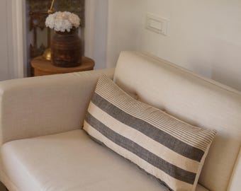 May include: A white couch with a black and white striped lumbar pillow. The pillow is made of a soft, textured fabric.