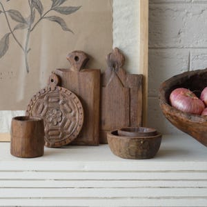 May include: A collection of rustic wooden kitchenware, including cutting boards, bowls, and a small cup. The cutting boards have unique shapes and carved details. A wooden bowl holds several red onions. The items are arranged on a white surface.