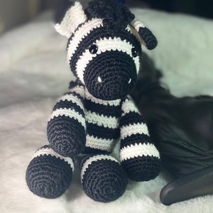 Könnte beinhalten: Ein gestricktes Zebra-Plüschtier mit schwarzen und weißen Streifen. Das Zebra hat schwarze Augen und eine weiße Nase.