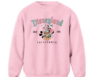 Puede incluir: Una sudadera de cuello redondo en color rosa claro con un gráfico de Mickey Mouse, Minnie Mouse, Donald Duck, Daisy Duck y Goofy. El texto dice Disneyland, EST 1955 y CALIFORNIA en una mezcla de colores pastel y letras negras.