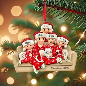 Puede incluir: Un adorno navideño que representa a una familia de cinco miembros, todos con pijamas rojos y gorros de Papá Noel. El adorno incluye los nombres Mia, Dad, Mum, Freya y Rose. La familia sostiene un gato blanco. El adorno dice "Christmas 2026".