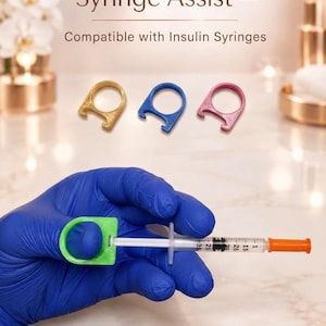 Può includere: ThumbMate Syringe Assist, compatibile con siringhe da insulina. Il set include strumenti in plastica a forma di anello nei colori oro, blu e rosa. Un anello verde è fissato allo stantuffo di una siringa in plastica con tappo arancione.