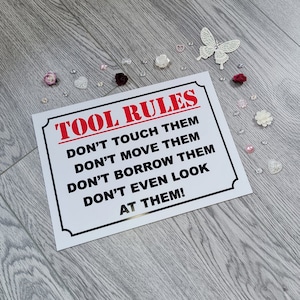 May include: White sign with black text and red title "TOOL RULES". The sign has five rules written in all caps: "DON'T TOUCH THEM", "DON'T MOVE THEM", "DON'T BORROW THEM", "DON'T EVEN LOOK", and "AT THEM!"