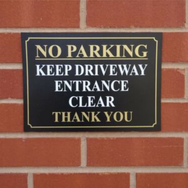 May include: Black and gold sign with white text that reads "No Parking Keep Driveway Entrance Clear Thank You".