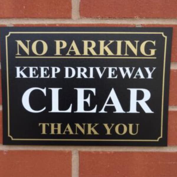 May include: Black and gold sign with the text "No Parking Keep Driveway Clear Thank You".