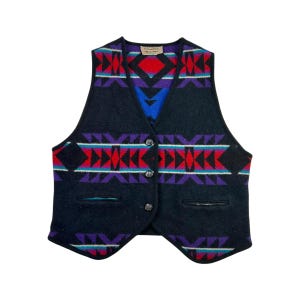 May include: Black wool vest with a Southwestern geometric pattern in red, purple, turquoise, and black. The vest has a V-neck, three buttons, and two front pockets. A small tag is visible at the neckline.