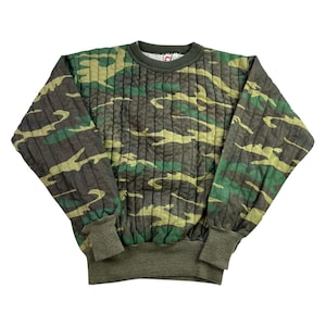 May include: A camouflage-patterned sweatshirt in shades of green, brown, and yellow. The long-sleeved top features a ribbed crew neck, cuffs, and hem. The fabric has a quilted texture.