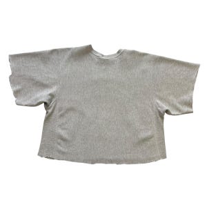 Puede incluir: Una sudadera gris claro de manga corta con cuello redondo. Las mangas y el dobladillo inferior tienen un borde en bruto sin terminar. La tela tiene una textura acanalada. La camisa est&aacute; tendida sobre un fondo blanco.