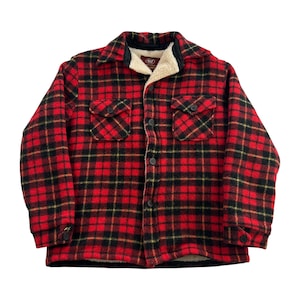 May include: A red and black plaid flannel shirt jacket with a cream-colored sherpa lining on the collar and inside. The jacket has two chest pockets, black buttons, and buttoned cuffs. The jacket is a classic style.
