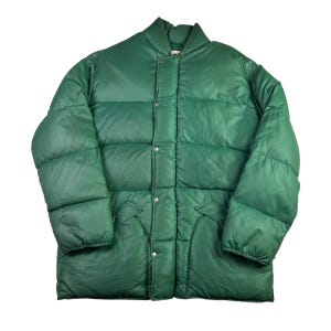Puede incluir: Chaqueta acolchada verde con diseño acolchado. La chaqueta tiene cuello alto, cierres de botón a presión y dos bolsillos delanteros. La chaqueta es de color verde liso y vibrante.