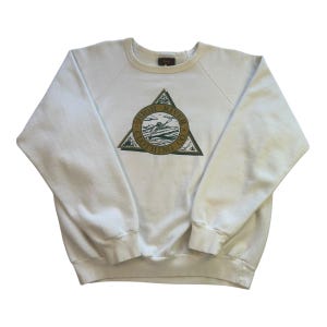 May include: A cream-coloured sweatshirt with a crew neck and long sleeves. The front displays a green and gold triangle design with the words "HIGH RIVER CLOTHING CO." around a surfer graphic.
