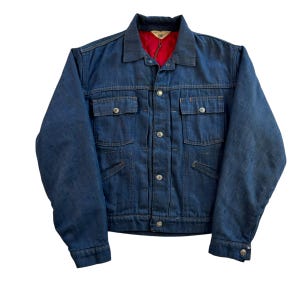 May include: A vintage denim jacket in a dark blue wash. It has a red quilted lining, four front pockets, and silver button closures. The collar is classic, and the jacket shows signs of wear. The jacket is a classic style.