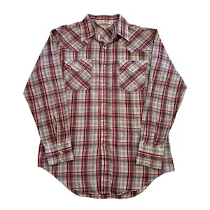 May include: A long-sleeved plaid shirt in red, white, and grey. The shirt has two chest pockets with decorative stitching and pearl snap closures. The collar and cuffs are also detailed. The shirt is made by McGregor.