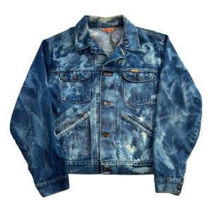 May include: A vintage denim jacket with a unique blue and white tie-dye pattern. The jacket features two chest pockets, two side pockets, and button closures. The collar is a classic style, and the jacket has a distressed look.