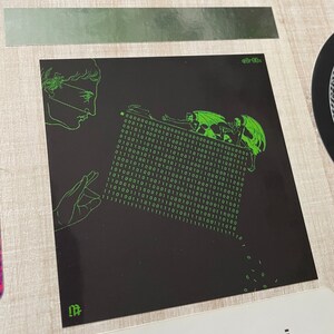 Puede incluir: Una pegatina negra y verde con un gr&aacute;fico de una persona con un antifaz y una criatura con alas y cuernos. La criatura est&aacute; escalando una pared de c&oacute;digo binario. La pegatina tiene el texto "@8r00x" en la esquina superior derecha.