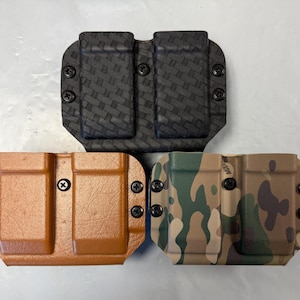 May include: Three double magazine pouches in different colors and patterns. The pouches are made of a textured material and have black screws. The pouches are arranged in a triangle shape.