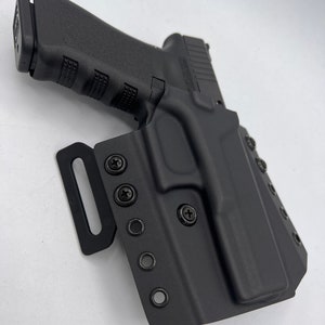 Puede incluir: Funda de pistola de polímero negro con trabillas de cinturón ajustables y múltiples agujeros para tornillos. La funda está diseñada para adaptarse a una pistola con un marco de polímero negro.