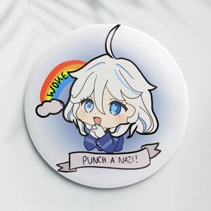 May include: A white button featuring an anime-style character with white hair and blue eyes, a rainbow, and the text "WOKE" and "PUNCH A NAZI!". The character is wearing a blue outfit.