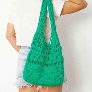 Puede incluir: Un bolso tote de ganchillo verde brillante con una correa ancha. El bolso tiene un diseño de tejido abierto con una base de ganchillo sólida. El bolso se lleva al hombro.