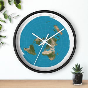 May include: A circular wall clock with a black frame. The clock face displays a flat-earth map design, with a blue backdrop and white grid lines. White clock hands show the time.