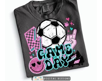 Könnte beinhalten: Ein anthrazitfarbenes T-Shirt mit einem Grafikdruck, der einen Fußball, einen rosa karierten Blitz, ein rosa Smiley-Gesicht mit Herzaugen, eine Hand mit einer Eins-Geste und einen Fußballschuh zeigt. Der Text GAME DAY ist in Schwarz gehalten.