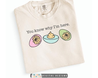May include: A cream-coloured t-shirt featuring the black text "You know why I'm here." and a graphic of three deviled eggs with pink, light blue, and light green egg white halves, each topped with a swirl of yellow yolk filling.