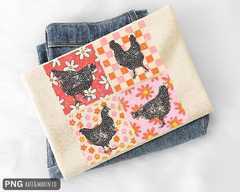 May include: A folded, cream-colored sweatshirt with a colorful chicken design. The design features four squares with a black chicken silhouette on a floral and checkered background. The sweatshirt is resting on a pair of blue jeans.