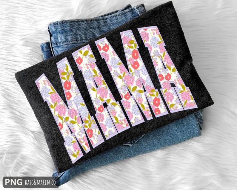 K&ouml;nnte beinhalten: Ein dunkelgraues T-Shirt mit dem Wort "MAMA" in gro&szlig;en Buchstaben mit floralem Muster. Die Buchstaben sind mit rosa, roten und lila Blumen gef&uuml;llt. Das T-Shirt liegt gefaltet auf einer Jeans.