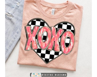 May include: A peach-colored t-shirt featuring a large heart graphic with a black and white checkered pattern. The text XOXO is printed in a pink and orange mottled, brushstroke-style font across the center of the heart. The shirt has a crew neckline.