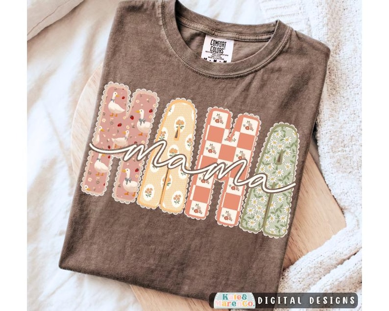 May include: A brown short-sleeve t-shirt featuring the word MAMA in large, scalloped-edge block letters. Each letter has a unique pattern: ducks on pink, floral on yellow, checkered on orange, and daisies on green. The word mama is written in white.