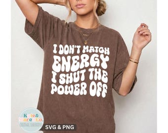 May include: A brown short-sleeved t-shirt featuring white text that reads I DON'T MATCH ENERGY I SHUT THE POWER OFF in a bold, wavy font. The shirt has a relaxed fit and a crew neckline. A small circular logo in the corner displays Kate & Maren Co.