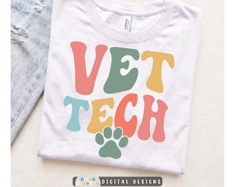 May include: A white short-sleeved t-shirt featuring the text VET TECH in large, wavy, multi-colored letters in shades of coral, sage green, and mustard yellow. Below the text is a solid sage green paw print graphic centered on the chest.