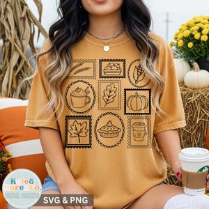 May include: A mustard yellow t-shirt featuring a black graphic print of nine rectangular and oval postage stamp-style frames. Each frame contains a different autumn-themed line drawing, including wheat, apples, corn, a mug, a leaf, a pumpkin, a maple leaf, a pie, and a coffee cup.