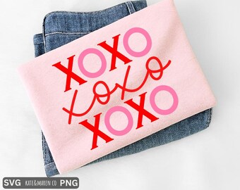 May include: A light pink t-shirt with the words "XOXO" in red and pink. The shirt is folded and resting on top of a pair of blue jeans. The text is in a playful, handwritten style, perfect for Valentine's Day or expressing affection.