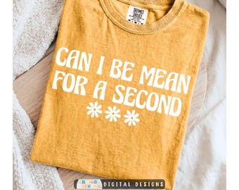 以下が含まれることがあります： マスタードイエローの半袖Tシャツで、クルーネック仕様です。フロントには白い文字で「CAN I BE MEAN FOR A SECOND」と書かれており、その下に3つの白いデイジーの花のアイコンが並んでいます。生地は少し使い古されたようなヴィンテージ感のある風合いです。