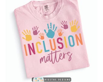 May include: A light pink t-shirt featuring a graphic of colorful handprints in yellow, purple, orange, and blue above the text INCLUSION matters in multi-colored block and script lettering. The shirt has a Comfort Colors brand label.