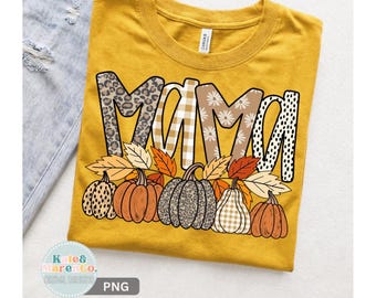 May include: A mustard yellow t-shirt featuring the word MAMA in large letters with varied patterns including leopard print, beige gingham, daisies, and black dots, layered over a row of pumpkins and autumn leaves in orange, brown, and tan.
