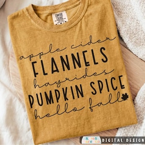 May include: A mustard yellow short-sleeve t-shirt featuring black text that reads apple cider, FLANNELS, hayrides, PUMPKIN SPICE, and hello fall, with a small maple leaf icon next to the final line of text and a Comfort Colors brand neck label.