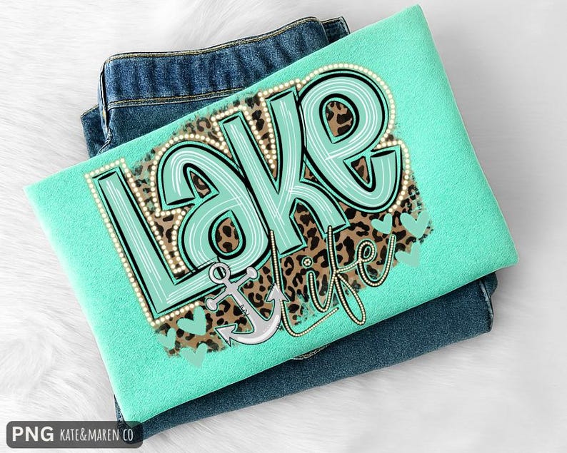 May include: A mint green t-shirt featuring a graphic print with the text "LAKE LIFE" in large, light blue letters outlined in white dots. The design includes a brown leopard print background, a gray anchor, and several small light blue hearts.